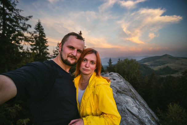 Couple hikers taking a selfie on top of a mountain, summer sunset time. Man and woman looking at beautiful inspirational landscape view, Carpathians mountains, Ukraine - Foto, afbeelding