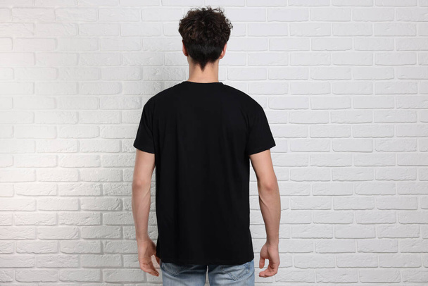 Man wearing black t-shirt near white brick wall, back view. Mockup for design - Photo, Image