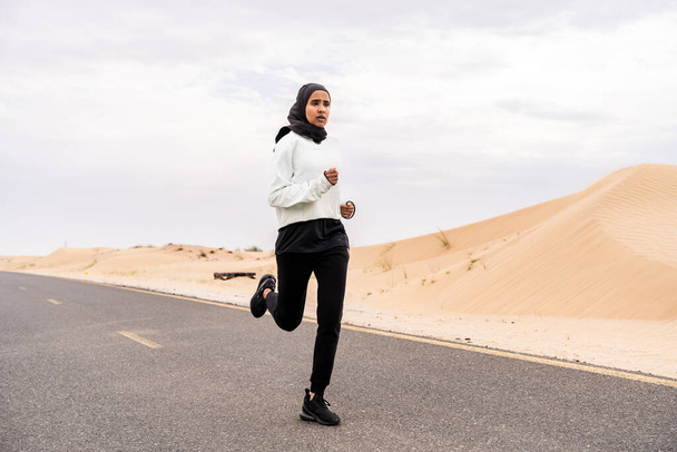 Beautiful middle-eastern arab woman wearing hijab training outdoors in a desert area - Sportive athletic muslim adult female wearing burkini sportswear doing fitness workout - Foto, afbeelding