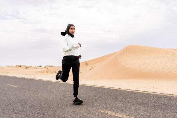 Beautiful middle-eastern arab woman wearing hijab training outdoors in a desert area - Sportive athletic muslim adult female wearing burkini sportswear doing fitness workout - Valokuva, kuva