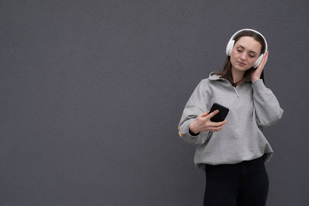 Lustige Studentin im grauen Sweatshirt, isoliert auf grauem Hintergrund, Selfie mit dem Handy, winkender Handgruß, Schulbildung im Hochschulkonzept. - Foto, Bild