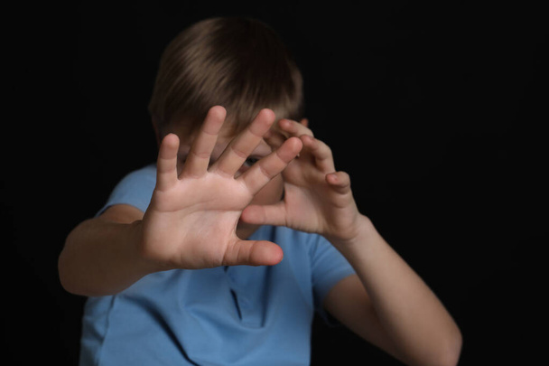 Boy making stop gesture against black background, focus on hands. Children's bullying - Fotó, kép