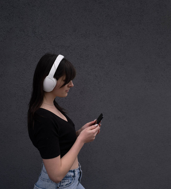 Lächelnde kaukasische junge Frau hört Rockband-Sänger E-Book-Podcast über Kopfhörer und wählt Tonspur auf Handy auf grauem Hintergrund - Foto, Bild