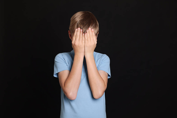 Boy covering face with hands on black background. Children's bullying - Photo, Image