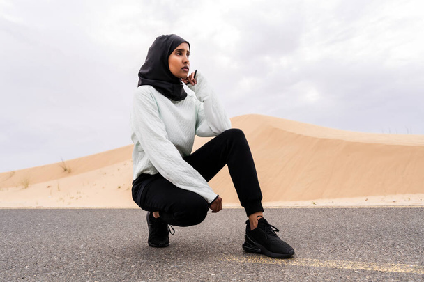 Όμορφη γυναίκα από τη Μέση Ανατολή με χιτζάμπ σε εξωτερικούς χώρους σε μια περιοχή της ερήμου - Αθλητική μουσουλμάνα ενήλικη γυναίκα φορώντας μπούρκιν αθλητικά κάνοντας γυμναστική γυμναστικής - Φωτογραφία, εικόνα