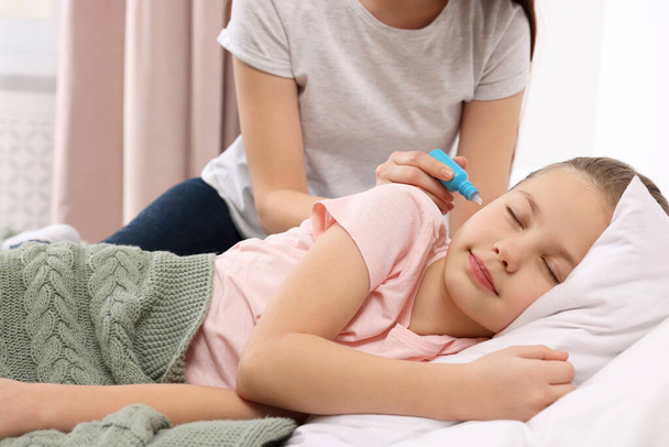 Mother dripping medication into daughter's ear in bedroom - Foto, Imagen
