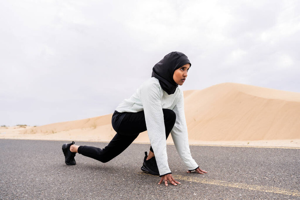 Beautiful middle-eastern arab woman wearing hijab training outdoors in a desert area - Sportive athletic muslim adult female wearing burkini sportswear doing fitness workout - Фото, изображение