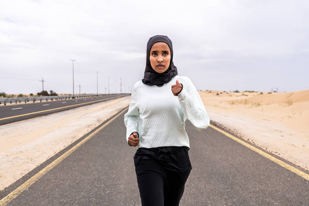 Beautiful middle-eastern arab woman wearing hijab training outdoors in a desert area - Sportive athletic muslim adult female wearing burkini sportswear doing fitness workout - Фото, зображення