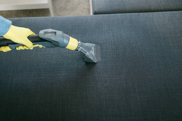 Cleaning service company employee removing dirt from furniture in flat with professional equipment. Man arm cleaning sofa with washing vacuum cleaner - Фото, зображення