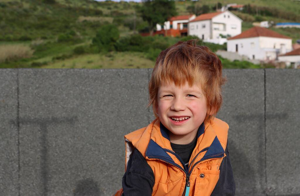 O menino loiro estreita os olhos e olha diretamente para a câmera. Feliz menino de cinco anos. - Foto, Imagem