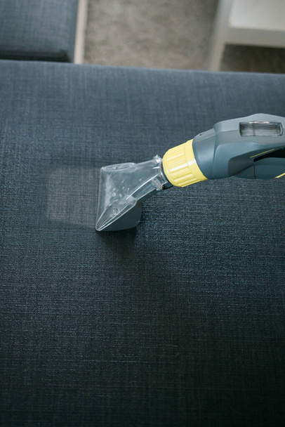 Siivouspalvelun työntekijä poistaa likaa huonekaluista litteässä ammattikäyttöön tarkoitetuilla laitteilla. Mies käsi puhdistus sohva pesu pölynimuri - Valokuva, kuva
