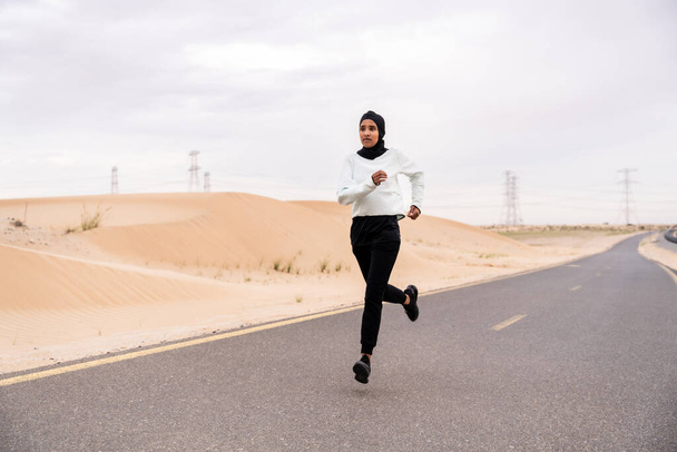 Beautiful middle-eastern arab woman wearing hijab training outdoors in a desert area - Sportive athletic muslim adult female wearing burkini sportswear doing fitness workout - Фото, изображение
