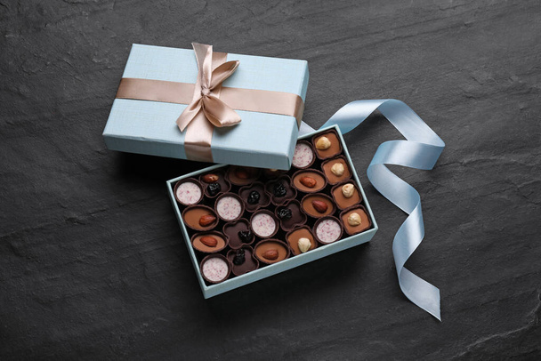 Open box of delicious chocolate candies and light blue ribbon on black table, flat lay - Fotoğraf, Görsel