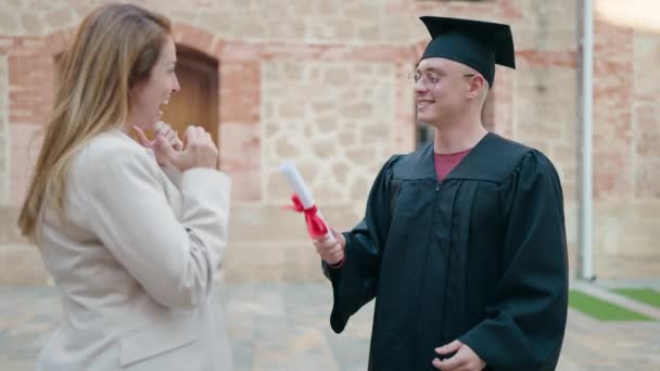 Man and woman mother and son hugging each other celebrating graduation at university - Materiał filmowy, wideo