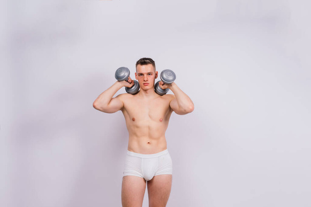 Shirtless bodybuilder holding a dumbell and showing his muscular arms. - Foto, Bild