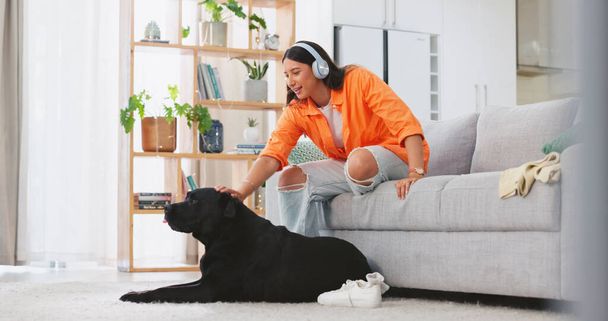 Phone, headphones and laughing woman with dog on sofa in home living room. Comic, relax and happy female streaming music, radio or podcast with smartphone while playing with animal, pet or bonding - Photo, image