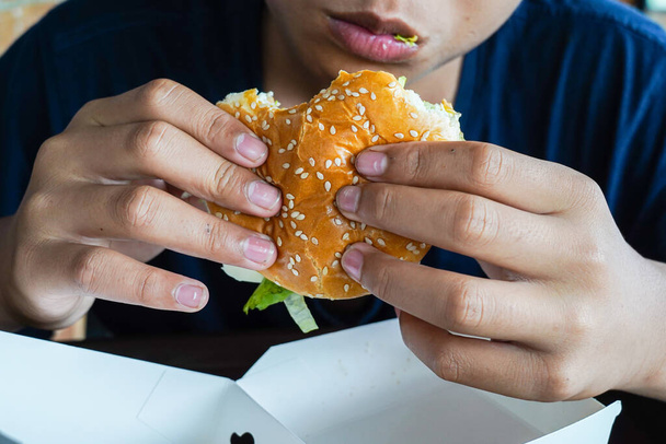 hamburger w ręce chłopca, głodny chłopiec trzyma cheeseburgera przed jedzeniem go, przestrzeń skopiować - Zdjęcie, obraz