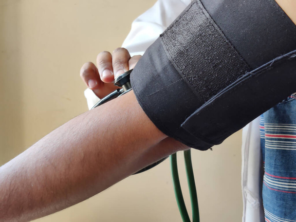 Immagine di un medico che indossa un grembiule bianco che esamina la pressione sanguigna di un paziente - Foto, immagini