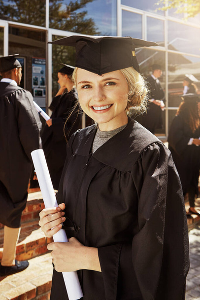 Este es mi boleto para una gran carrera. Retrato de una estudiante universitaria sonriente sosteniendo su diploma afuera el día de la graduación - Foto, imagen