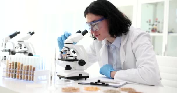 Long-haired man finishes studying grains under microscope leaning on back of chair. Laboratory worker feels happy to complete task slow motion - Footage, Video