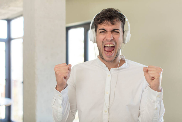 young handsome man feeling shocked,laughing and celebrating success. listening music with headphones - Foto, Bild