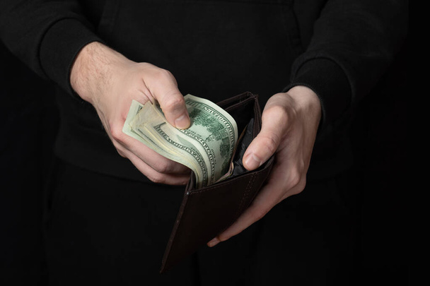 Un hombre saca dinero de su cartera sobre un fondo negro oscuro. - Foto, imagen