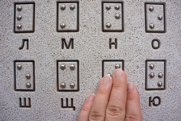 La mano de la mujer está leyendo Braille al aire libre de cerca. Lectura táctil de las letras del alfabeto ucraniano (cirílico) en braille en un parque público - Foto, Imagen