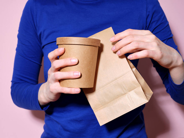 Woman dressed in bright blue t-shirt holding food delivery packaging - Zdjęcie, obraz