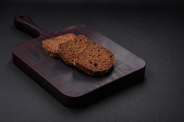 Loaf of fresh crispy brown bread with grains and seeds on dark concrete background - Foto, imagen