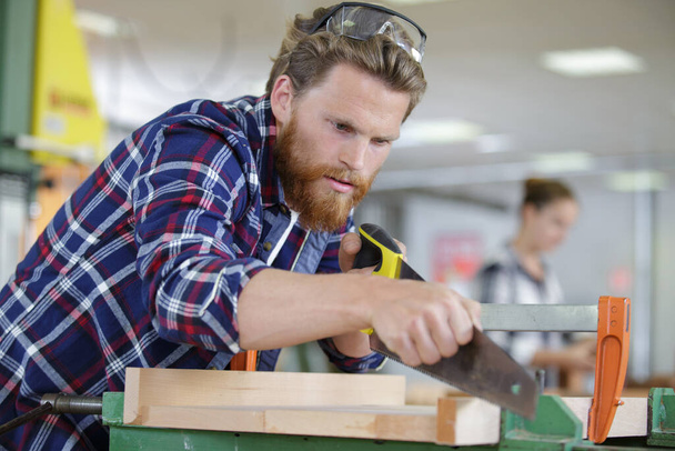 a man carpenter cuts a wooden beam using a handsaw - 写真・画像