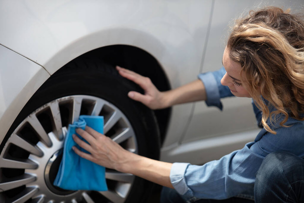 woman is cleaning the car tyre - Foto, afbeelding