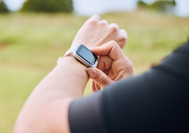 Hands, training and smart watch with a sports person outdoor, checking the time during a workout. Arm, exercise and technology with an athlete tracking cardio or endurance performance for fitness. - Photo, Image