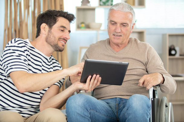 cheerful disabled man near handsome son looking at tablet - Foto, afbeelding