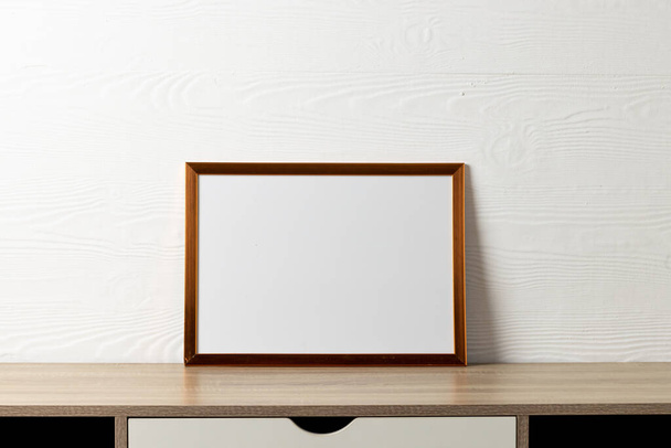 Brown empty frame with copy space on table against white wall. Mock up frame template, interior design and decoration. - Foto, imagen