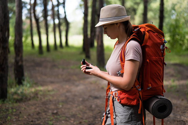 Young caucasian woman is hiking and using a compass in the forest - 写真・画像