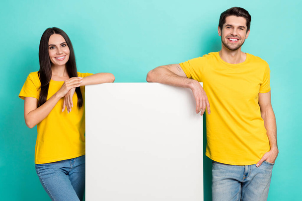 Photo of positive sweet married couple wear yellow t-shirts holding placard empty space isolated teal color background. - Foto, immagini