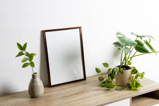 Black empty frame with copy space and plants in pots on table against white wall. Mock up frame template, interior design and decoration. - Fotografie, Obrázek