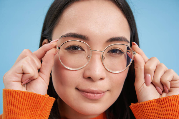 Close up portrait of amazed girl, looks closer at camera in glasses, standing against blue background. Copy space - Photo, Image