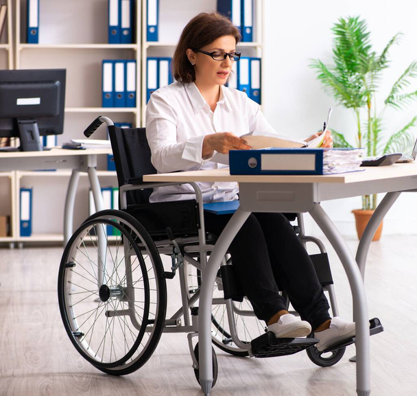 Работница в инвалидной коляске в офисе - Фото, изображение
