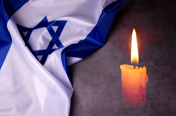 День памяти жертв Холокоста. Йом ха-Шоа. Яркая горящая свеча и официальный флаг Израиля на темно-сером фоне. День памяти евреев. - Фото, изображение