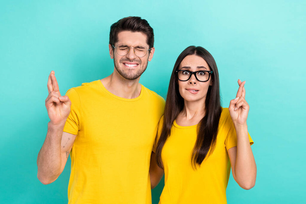 Photo of two young nervous people panic crossed fingers wait bite lips expectation wear glasses please isolated on aquamarine color background. - Foto, afbeelding