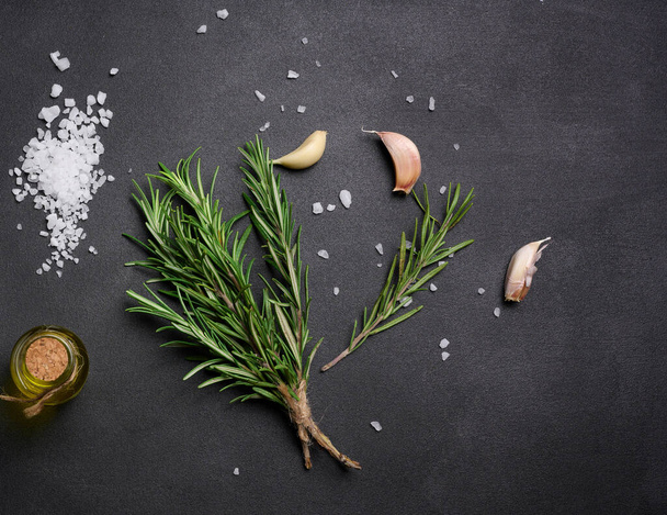 Sal blanca gruesa dispersa, granos de pimienta y ramitas de romero sobre una mesa negra, ingredientes para cocinar pescado y carne - Foto, imagen