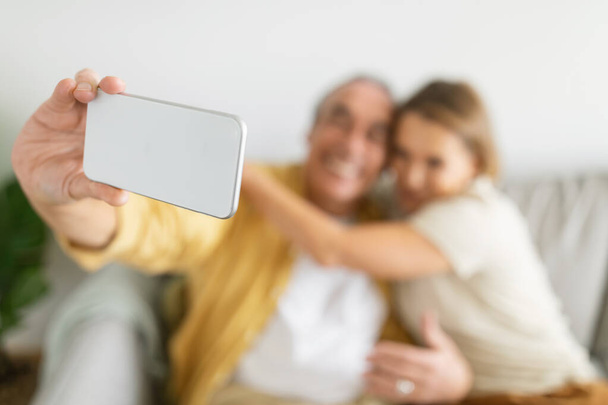 Elderly couple spending time, having fun and taking selfie on smartphone, spouses enjoying online entertainments, focus on phone. Older generation and modern tech concept - Photo, Image
