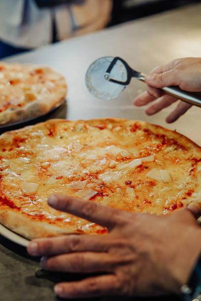 Stajyer şef pizza kesicisi ile harika bir iş çıkarıyor. Herkesin tadını çıkarması için lezzetli dilimler yapıyor. - Fotoğraf, Görsel