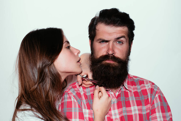 Barbershop procedures. Hairdresser concept. Woman hairdresser cuts beard with scissors. Man with long beard, mustache and stylish hair - 写真・画像