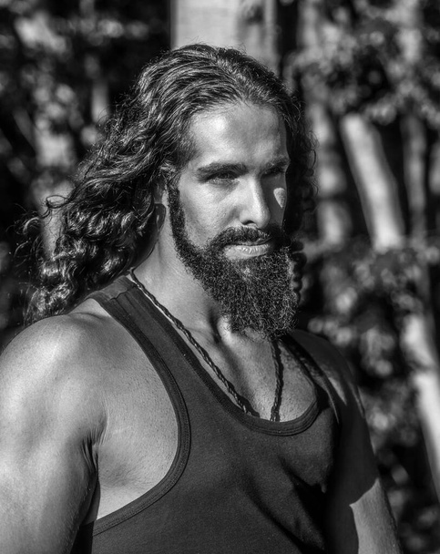 Handsome bearded man with long dark hair. Sexy bearded model man. Man fashion and style concept. Portrait of handsome young strong man with long dark hair looking away while standing at forest - Foto, Bild