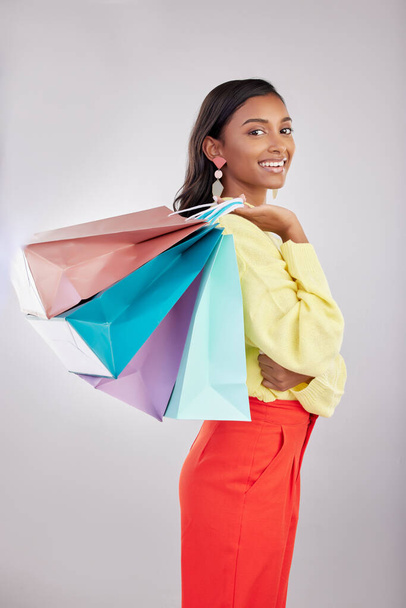Portrait, shopping and sales with a woman customer in studio on a gray background for retail or consumerism. Fashion, luxury or smile with an attractive young female carrying bags over her shoulder. - Foto, imagen