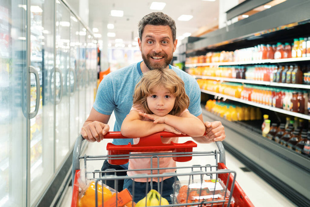 Amazed family father and child son with shopping cart buying food at grocery store or supermarket. Surprised face. Man shopper with groceries - Φωτογραφία, εικόνα