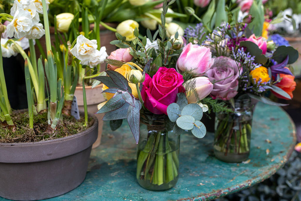 Spring modest bridal bouquet with red rose, eucalyptus, tulip, ranunculus in a glass jar on an iron table - Φωτογραφία, εικόνα