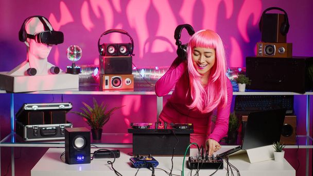 ターンテーブルでテクノミュージックを演奏する陽気なミュージシャンは、パーティー中にクラブで楽しさとダンスを楽しんでいます。プロのオーディオ機器を使用してリミックスサウンドを実行ピンクの髪を持つアーティスト - 写真・画像